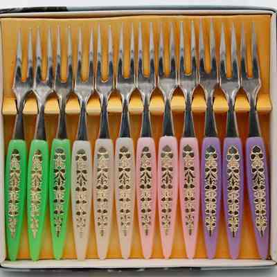 Japanese "Little Fork" set.: Up close image of the set of 12 little forks with purple, pink, white, and green handles and silver prongs. They sit in their original box with a yellow backing.