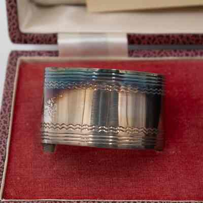 One of the silver napkin rings given to Mrs. Jessie Jordan by the Kuwait Masonic Lodge.: Up close image of one of the two silver napkin rings in a pink and black box with a red and white interior.