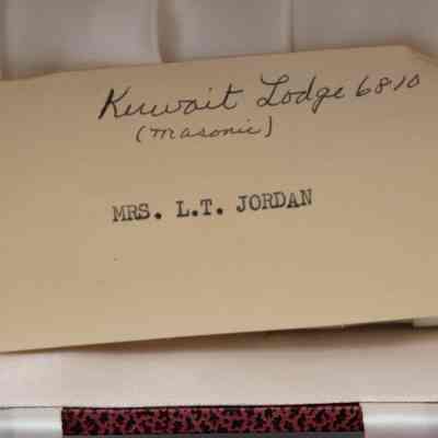 Note found in the box with the pair of napkin rings.: Up close image of the note found with the napkin rings. The note is on yellowed paper with black printed text and handwriting. The handwritten note reads "Kuwait Lodge 6810 (Masonic)" and the printed note reads "MRS. L.T. JORDAN."