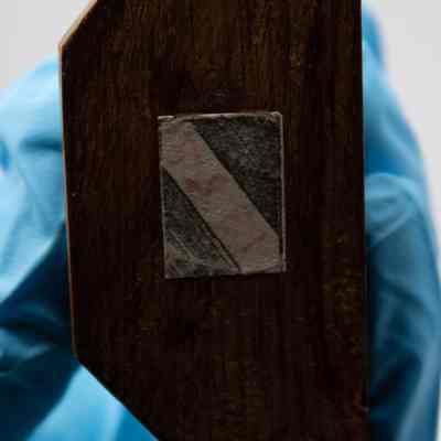 Bottom of the wooden base on the carved ivory figurine of St. George Slaying the Dragon from India.: Up close image of the bottom of the wooden base of the carved ivory figurine of St. George Slaying the Dragon. There is a faint rectangular sticker with red writing, reading "1355."