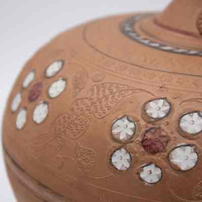 Decorations on the terracotta water jug given to the Jordans by Pakistani president Ayub Khan.: Up close image of the red and white raise floral motifs on the orange terracotta rounded water jug.