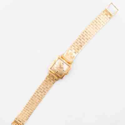 The 18K gold Omega Ladymatic watch given to Mrs. Jessie Jordan by Sheikh Abdullah Mubarak Al Sabah.: Image of the gold Omega Ladymatic wrist watch laying flat. The watch is square in shape with a gold watch face and numbers. The clock hands and watch band are also gold. There is a small Omega symbol on the clasp of the watch.