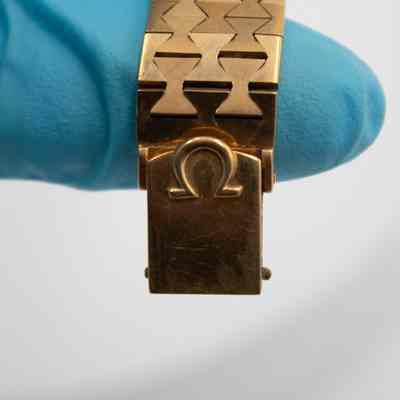 The rectangular clasp on the 18K gold Omega Ladymatic watch given to Mrs. Jessie Jordan by Sheikh Abdullah Mubarak Al Sabah.: Up close image of the rectangular watch clasp. There is a debossed gold Omega symbol.