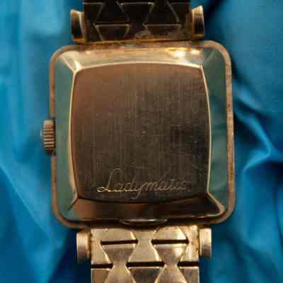 Back of the 18K gold Omega Ladymatic watch face.: Up close image of the back of the 18K gold Omega Ladymatic watch face. The face is square and the term "Ladymatic" is engraved on the back in cursive.
