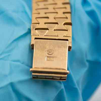 Back of the clasp on the 18K gold Omega Ladymatic watch.: Up close image of the back of the clasp on the gold watch. There is an embossed number and symbol.