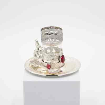 One of the cups, spoons, and saucers from the set.: Image of a set of one cup, spoon, and saucer. The cup is glass in a silver plated holder with an etched design and red gemstones. The plate and spoon are also silver plated.