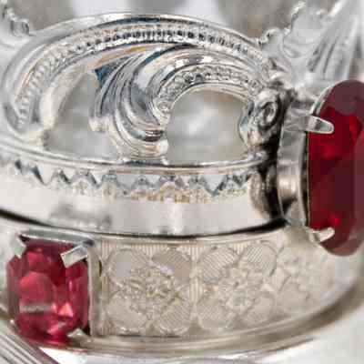 Plated silver base that holds the glass teacup.: Up close image of the plated silver base for the glass teacup. The base has red gemstones and a floral swirl design.