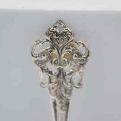 Handle of one of the silver plated spoons from the tea set.: Up close image of the end of the handle of one of the silver plated spoons. It is decorated with swirls.