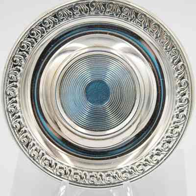 One of the silver plated saucers.: Up close image of one of the silver plated saucers. There is a pressed circular design in the center and a leaf and swirl design around the outer edge.