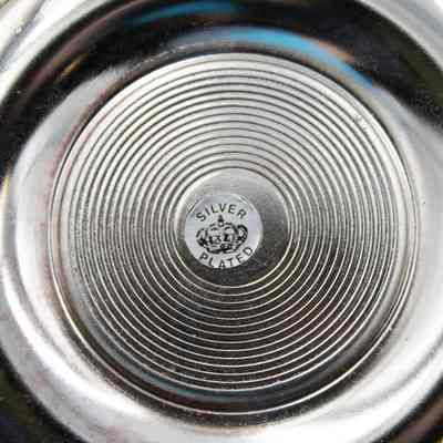 Back of one of the silver plated saucers.: Up close image of the back of one of the silver plated saucers. There is a pressed circular design in the middle and a silver sticker that reads "SILVER PLATED" in black text with a crown.