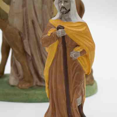 One of the male Bedouin figurines.: Up close image of one of the male figurines. He is wearing a brown traditional Kuwaiti dresses, yellow shall, and white head covering with a walking stick