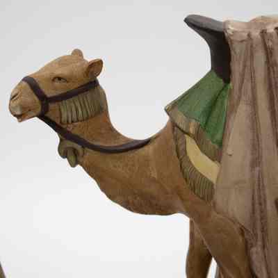 One of the Bedouin camel figurines.: Up close image of the head of one of the Bedouin camels. The camel is light brown and has brown reins with gold fringe detail. The green and yellow saddle blankets are also visible.
