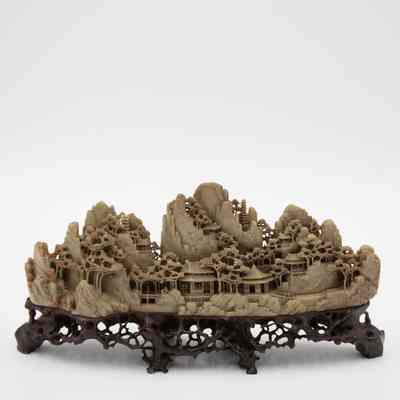 One of two grey stone-carved Shoushan villages.: Image of one of two grey-green stone carved villages on dark brown stands. The villages are Shoushan-style with trees, people, and Chinese houses.