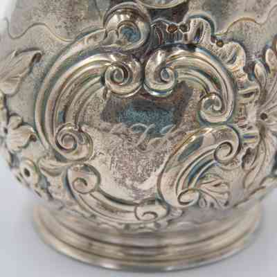 "LTJ," engraving into creamer: The silver creamer showcases detailed embossed floral and scroll, with "LTJ" engraved centrally.