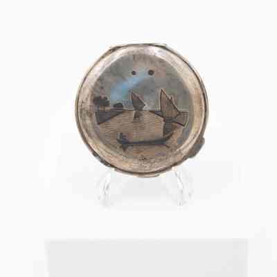 Back of compact: A silver compact features an etched dhow and palm trees.