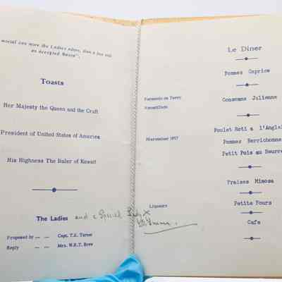 Inside the program from the 1961 Ladies' Festival at the Kuwait Masonic Lodge No. 6810.: Image of the inside the program listing the toasts for the night and menu in blue text. The left page reads "'No mortal can more the Ladies adore, than a free and an accepted Mason.'" at the top and then lists the "Toasts" for "Her Majesty the Queen and the Craft, President of the United States of America, His Highness The Ruler of Kuwait." It also lists "The Ladies, Proposed by ... ... Capt. T.H. Turner, Reply ... ... Mrs. W.R.T. Brew." There is also a handwritten note adding "and a Special Lady X [illegible cursive]." The right page has "Le Diner" listed, "Pommes Caprice," "Fernando de Terry Amontillado, Consomme Julienne," "Niersteiner 1957, Poulet Roti a l'Anglaise, Pomme Berrichonne, Petit Pois au Beurre," "Fraises Mimosa," "Liquers, Petite Fours," and "Cafe."