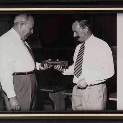Photograph of L.T. Jordan receiving miniature Yard of Ale: In the framed photograph, a man gives L.T. Jordan his miniature yard of ale. The photo is black and white, in a black frame.