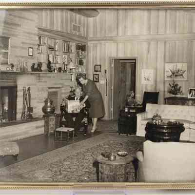 Photograph of L.T. and Jessie Jordan in their Lufkin Home: Jessie leans over a L.T. reading a magazine in their decorated living room, showcasing bookshelves and a large fireplace.