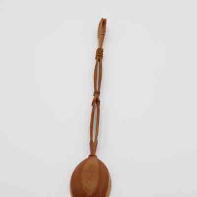 Carved Dark Brown Wooden Spoon: Close-up image of the spoon. The spoon's handle is separated into three sections. The first two are oblong shapes that are open in the middle. The very end of the handle is another oblong carving, this time smaller.