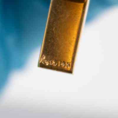 Close up on text on tie bar: The edge of the bar, it has unreadable markings next to "14K."