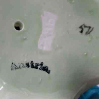 Bottom of the 19th century green ceramic vase made in Austria.: Up close image of the bottom of the green ceramic vase. The bottom is mint green and has the word "Austria" stamped in black. There is also the number "57" stamped in black and a small hole drilled in, which would have been used to prevent cracking during firing in the kiln.