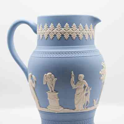 Wedgwood Jasperware pitcher: The Wedgwood blue Jasperware pitcher features intricate white relief designs. This side of the pitcher features a woman with a deer, as well as a cherub on a pedestal.