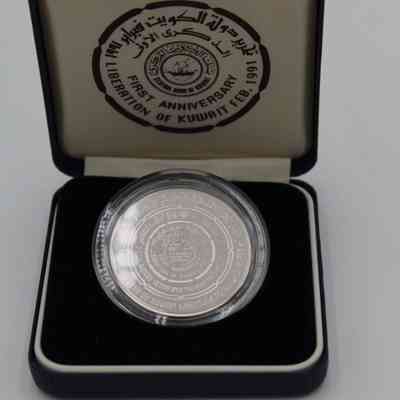 Inside of Box: Image of the box's interior. The inside of the box's top is white and has a black stamp in the middle. In the stamp in black capital letters the bottom half reads "Central Bank of Kuwait | First Anniversary | Liberation of Kuwait  Feb. 1991." The top half of the stamp has the same message but in Arabic. In the middle of the stamp is a depiction of a dhow.