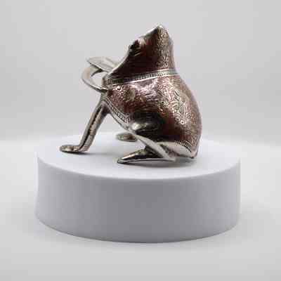 Backside of frog ashtray: A silver frog ashtray with a wide mouth and tongue cigarette rest features intricate red line designs.