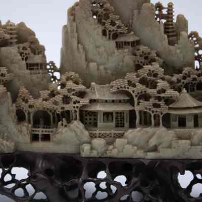 Grey stone-carved Shoushan village.: Up close image of part of one of the grey-green stone carved villages on dark brown stands. The villages are Shoushan-style with trees, people, and Chinese houses.