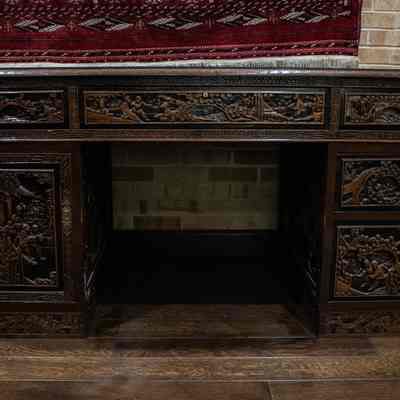 Wooden desk: The image shows an intricately carved wooden desk with detailed Hong Kong-themed designs on its drawers and sides, set against a brick wall backdrop.