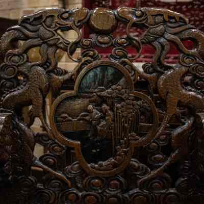 Decorations on back of wooden chair: The intricately carved wooden chair back features detailed dragon designs and an inlaid scene.