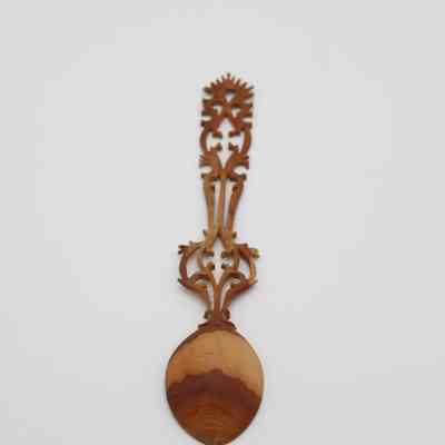 Back of light brown wooden spoon: The image shows an intricately carved, light brown wooden spoon resting on a plain surface.