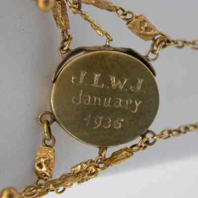 Engraving on the back of the gold floral locket.: Up close image of the back of the gold floral locket engraved with "J.L.W.J. January 1936."