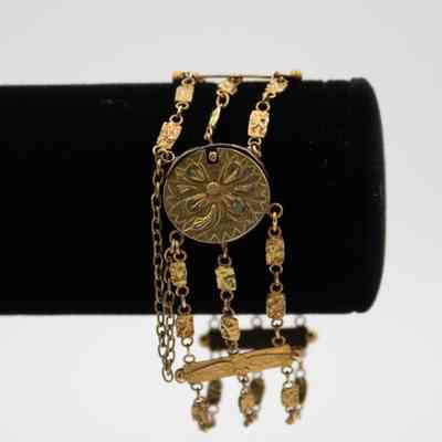 Gold bracelet with locket that belonged to Mrs. Jessie Jordan.: Image of the gold floral locket with three chains on a black bracelet display.