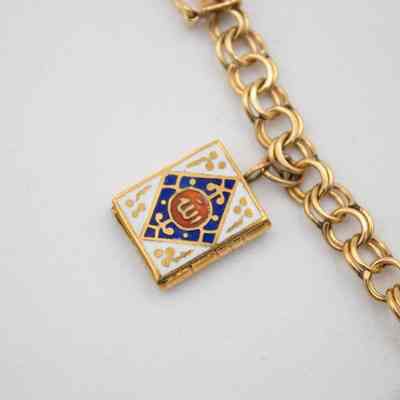 Book charm on Mrs. Jessie Jordan's gold charm bracelet.: Up close image of the small book charm on the gold bracelet. The book is gold and decorated with an red, white, and blue enamel cover.