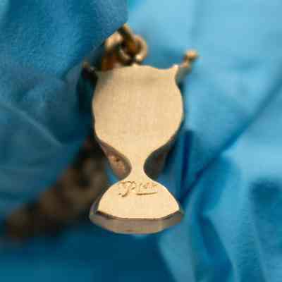 Back of the charm of the bust of a boy on Mrs. Jessie Jordan's gold charm bracelet.: Up close image of the back of the gold charm of a bust of a boy with a crown. It is engraved with "R" and then "14K."