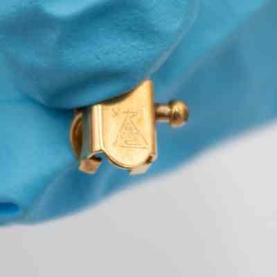 Back of the clasp of Mrs. Jessie Jordan's gold charm bracelet.: Up close image of the back of the clasp of the charm bracelet. It is engraved with a triangle with the letters "POLL" and "CR" inside. There is also "14K" engraved under the triangle.