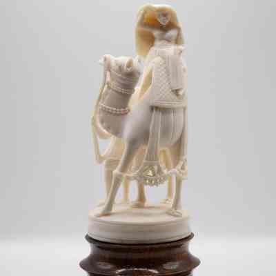 Small carved ivory statuette of a woman on camel with man leading camel on wooden base.: Front image of the small carved ivory statuette of a woman on camel with man leading camel on wooden base.