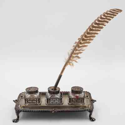 Full quill and ink stand: An elegant ink stand holds three vintage ink bottles, with a patterned quill resting.