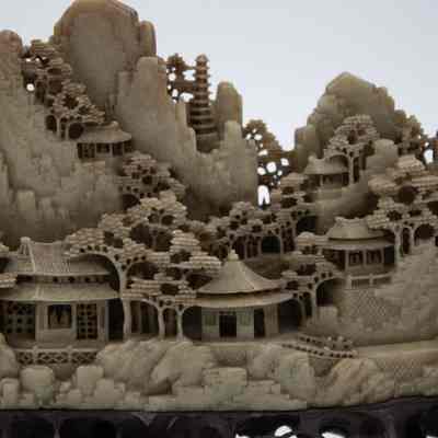 Grey stone-carved Shoushan village.: Up close image of part of one of the grey-green stone carved villages on dark brown stands. The villages are Shoushan-style with trees, people, and Chinese houses.