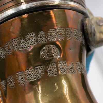 Text on coffee pot: A copper coffee pot with leather-wrapped handle, brass details, and stamped Arabic script.
