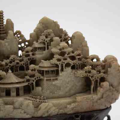 Grey stone-carved Shoushan village.: Up close image of part of one of the grey-green stone carved villages on dark brown stands. The villages are Shoushan-style with trees, people, and Chinese houses.