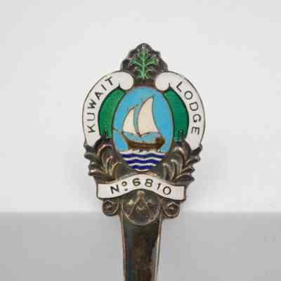 Handle of silver souvenir spoon from Kuwait Masonic Lodge 6810.: Up close image of the seal of Kuwait Masonic Lodge No. 6810 on the handle of the small silver souvenir spoon. The seal contains a Kuwaiti dhow and the traditional Freemason square and compass. It also reads "KUWAIT LODGE NO. 6810."