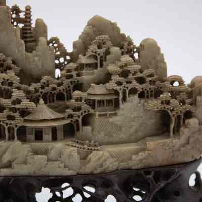Grey stone-carved Shoushan village.: Up close image of part of one of the grey-green stone carved villages on dark brown stands. The villages are Shoushan-style with trees, people, and Chinese houses.