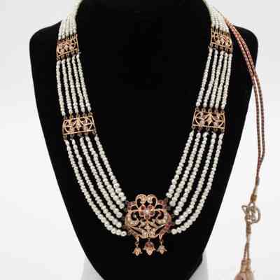 Gold and pearl necklace with ruby and diamond stones given to Mrs. Jessie Jordan by Her Highness Sheikha Badriah Al-Ahmad Al-Jaber Al-Mubarak Al-Sabah.: Image of the gold and pearl necklace with ruby and diamond stones on a faux black felt neck. There are 5 pearl strands of thin strands Persian Gulf pearls connected by gold appliques with red gemstones and white diamonds. There is a pair of cord coming from the back clasp with two tassels. The necklace also has an accompanying matching pair of gulf pearl drop earrings sitting on top of the faux neck.