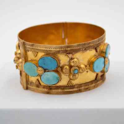 Gold cuff bracelet that was given to Mrs. Jessie Jordan by Sheikha Bebe Salim Al-Sabah.: Up close image of the large gold cuff bracelet set with blue turquoise stones and decorated with debossed gold details.