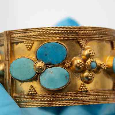 Gold cuff bracelet that was given to Mrs. Jessie Jordan by Sheikha Bebe Salim Al-Sabah.: Up close image of the large gold cuff bracelet set with blue turquoise stones and decorated with debossed gold details.