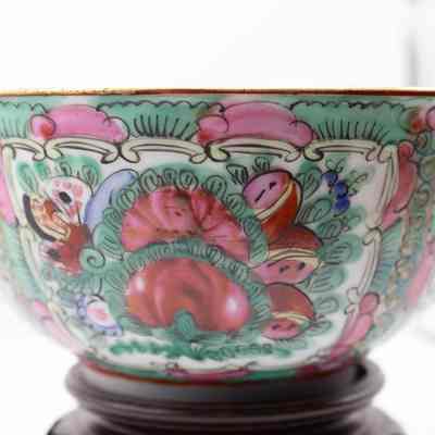 Bowl: The image showcases a gold-rimmed, hand-painted Hong Kong green bowl featuring intricate floral designs, resting on a polished teakwood stand.