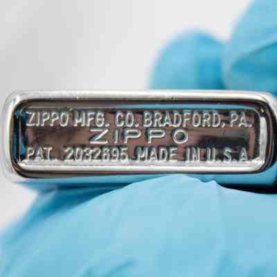 Bottom of a lighter with engraved information.: The bottom of the steel lighter. Three rows of text state "ZIPPO MFG. CO. BRADFORD, PA. ZIPPO. PAT 2032695 MADE IN U.S.A"