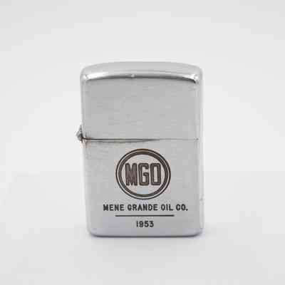 Mene Grande Oil Company Zippo: The steel lighter body has a circle with MGO inside, the Mene Grande Oil Company logo. Underneath it says "MENE GRANDE OIL CO. 1953." There is some wear on the metal near the hinge between the cap and body.